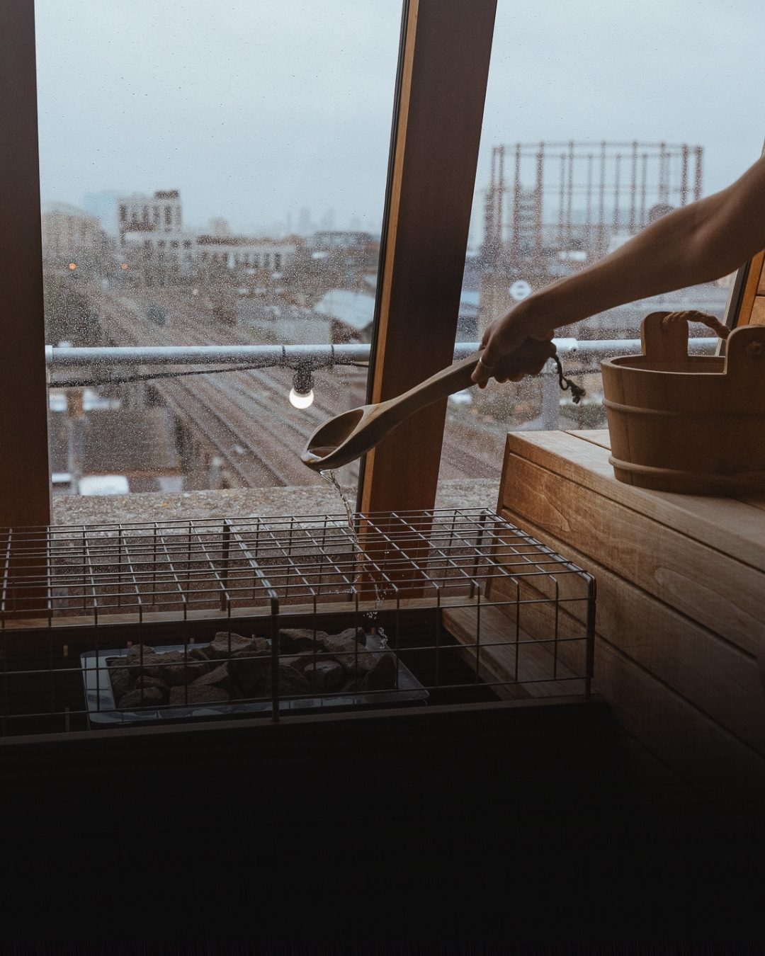 Pouring water on the sauna stones, with a rain-streaked view across Hackney