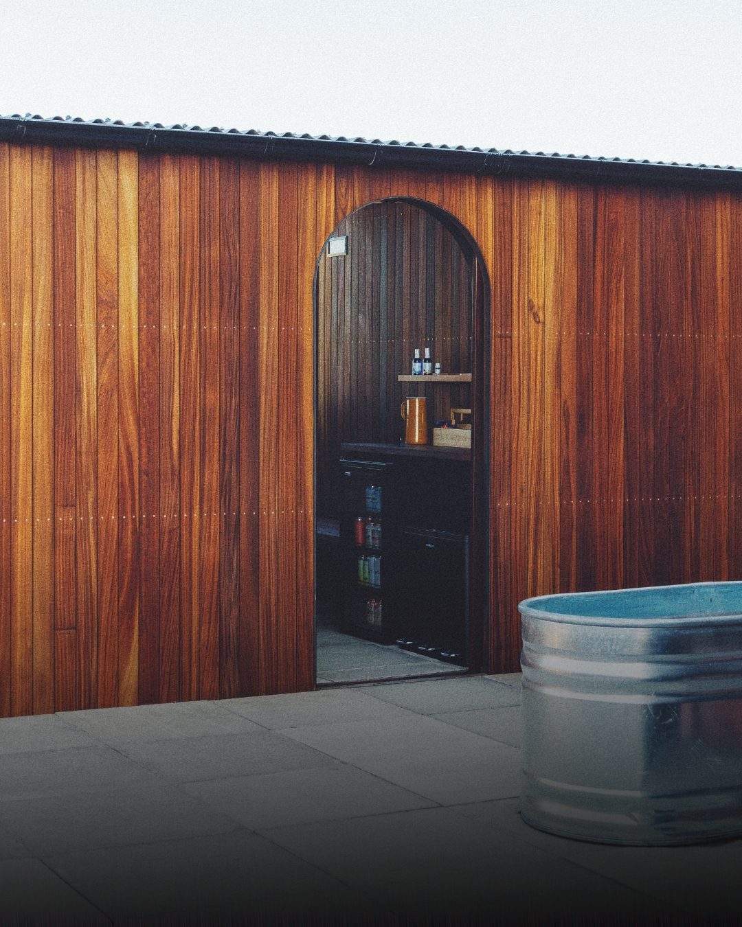 Arched doorway into a timber sauna cabin, with a cold plunge tub
